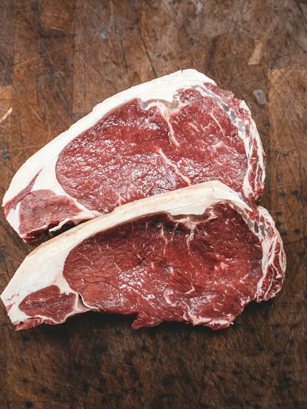 Dois bifes crus sobre uma tábua de madeira escura