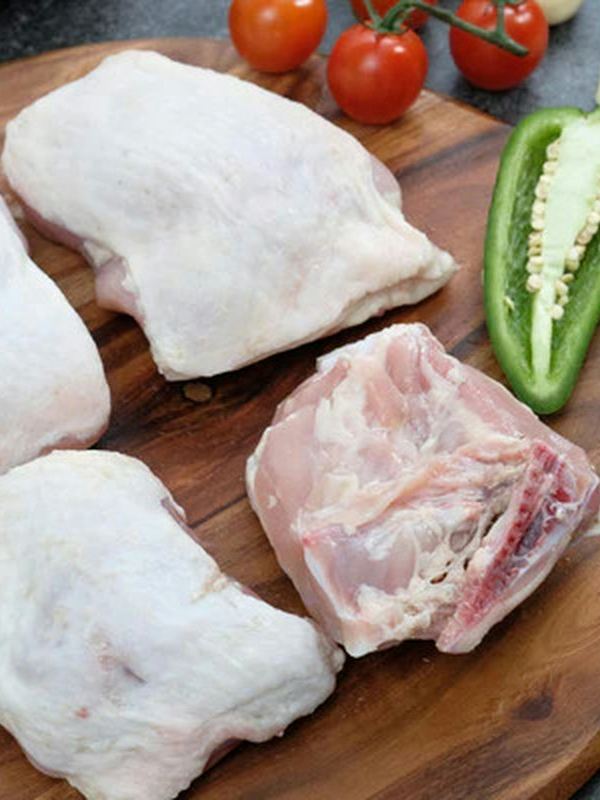 Pedaços de frango cru numa tábua com pimentas e tomates